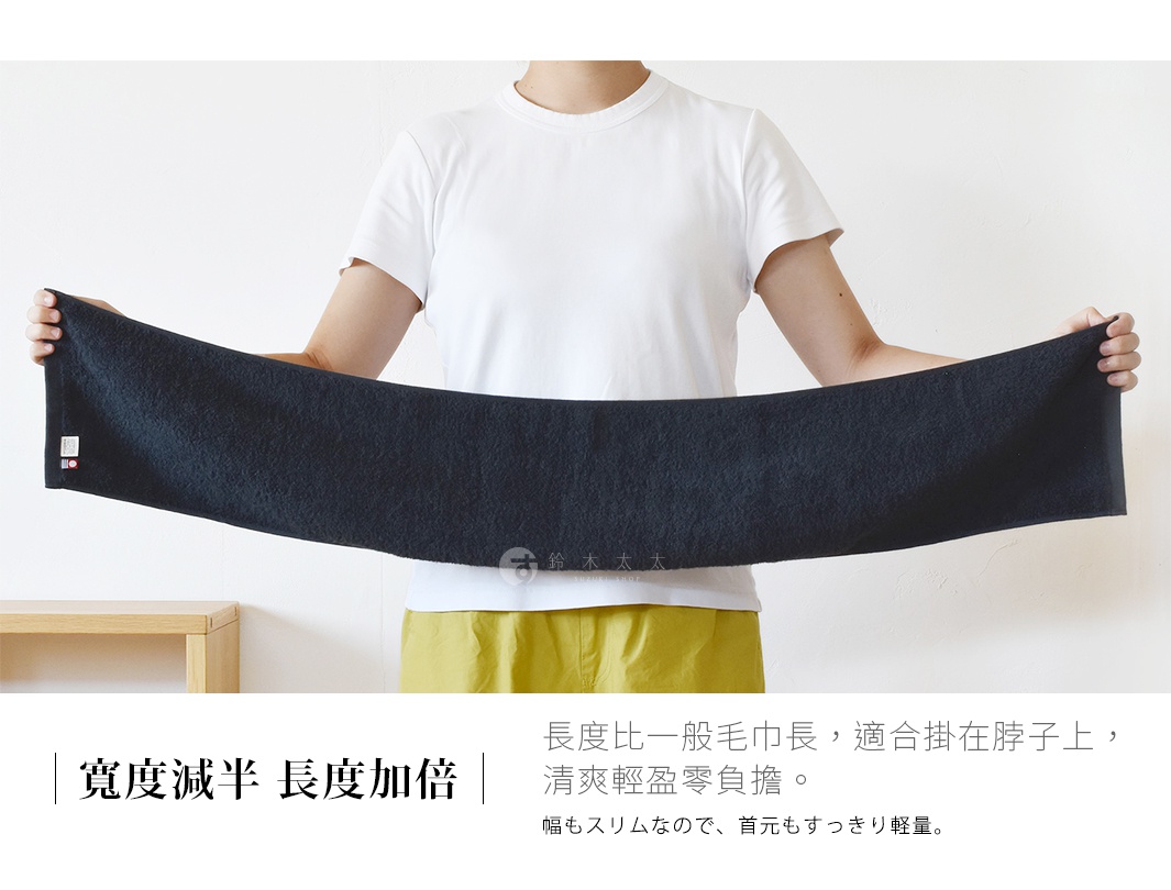 一位身穿白色短袖上衣與黃色裙裝的女性，雙手橫向展開一條深藍色的長條型毛巾。該毛巾設計細長，適合掛在脖子上使用，整體呈現簡約清爽的視覺風格，圖片下方並標註有說明該款毛巾特色為寬度減半、長度加倍的文字資訊。