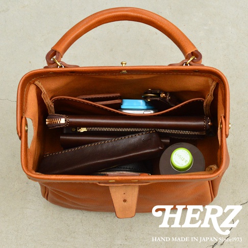 職人手作皮革Organ兩用方形口金托特包，淺棕色皮革，內部物品包含手機、錢包、筆等，結構清晰，設計實用。