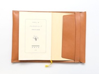 職人手作皮革翻蓋記事本書套，採用棕褐色光滑皮革製成，內含一本淺米色封面書籍，書套右側有一個內袋，左側則為書本放置區，整體風格簡約。