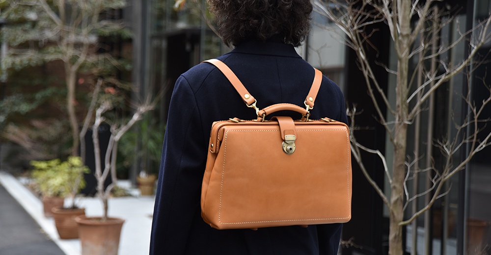 棕色皮革製作的復古醫生包造型三用背包，配有可調整的肩帶，可肩背或後背，包包正前方有金屬鎖扣與皮革束帶。