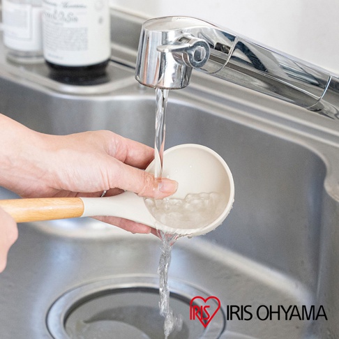 奶油色矽膠湯勺，配有木質手柄，在水龍頭下沖洗。