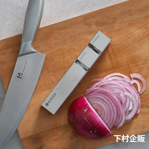 不鏽鋼磨刀器，印有 ESSYO 品牌標誌，旁邊有一把銀色不鏽鋼刀具和切片的紫洋蔥，放置於木質砧板上。