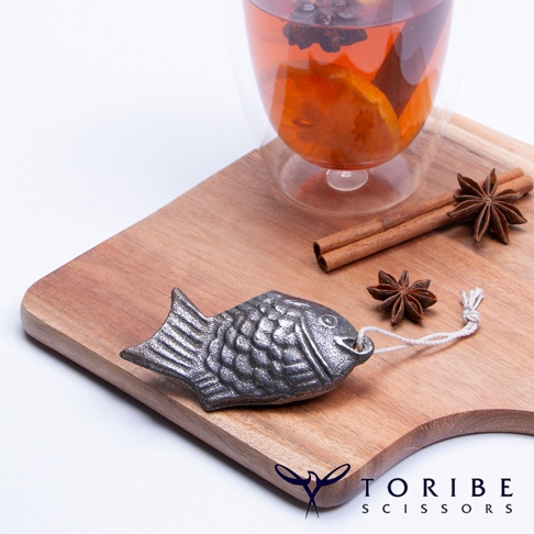 銀灰色、魚形狀的補鐵小鯛魚，帶有白色細繩，放置在木質砧板上，旁邊有肉桂棒和八角。