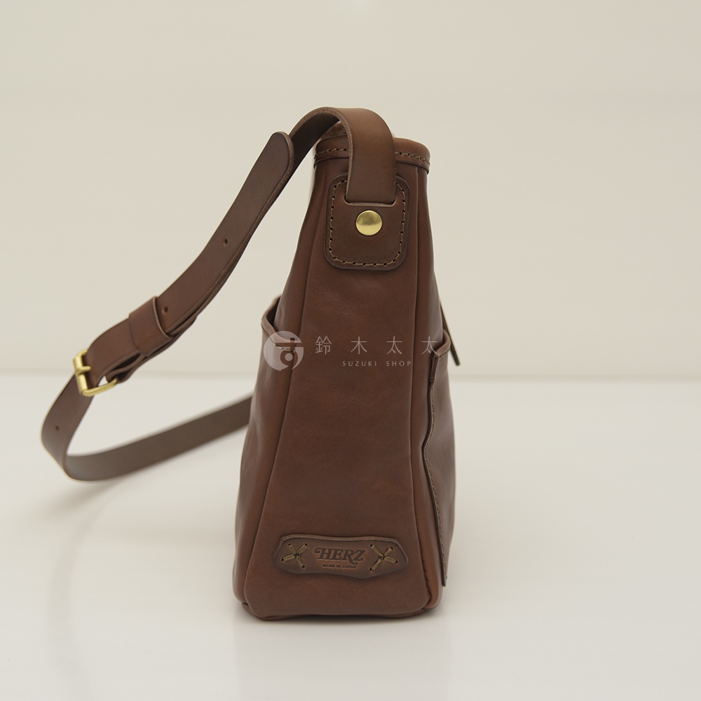 職人手作皮革輕便單肩側背包，呈現溫潤的棕色調，材質為天然皮革。包款側面有品牌壓紋。