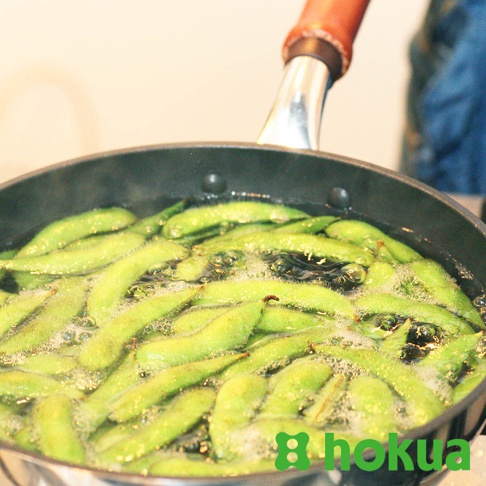 綠色毛豆在冒泡的水中翻滾，鍋子為黑色，配有木柄。