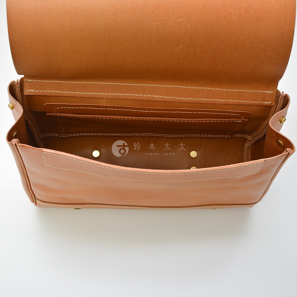 打開的棕色皮革包內部，可見內袋隔層和品牌標誌「SUZUKI SHOP」。