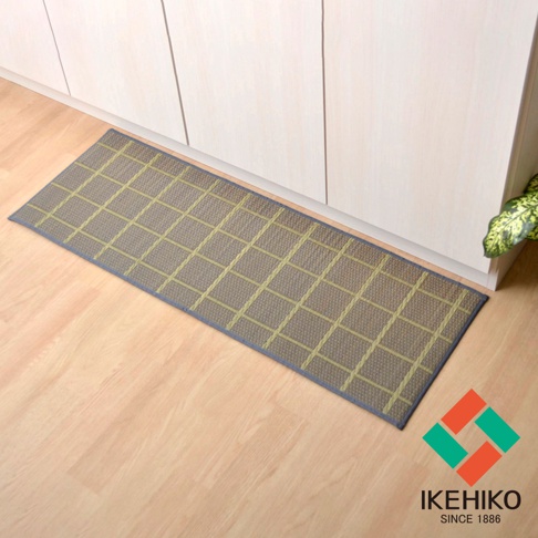 藺草編織的長方形廚房地墊，表面有綠色格紋，深藍色滾邊，置於淺木紋地板上，背景為白色櫥櫃。