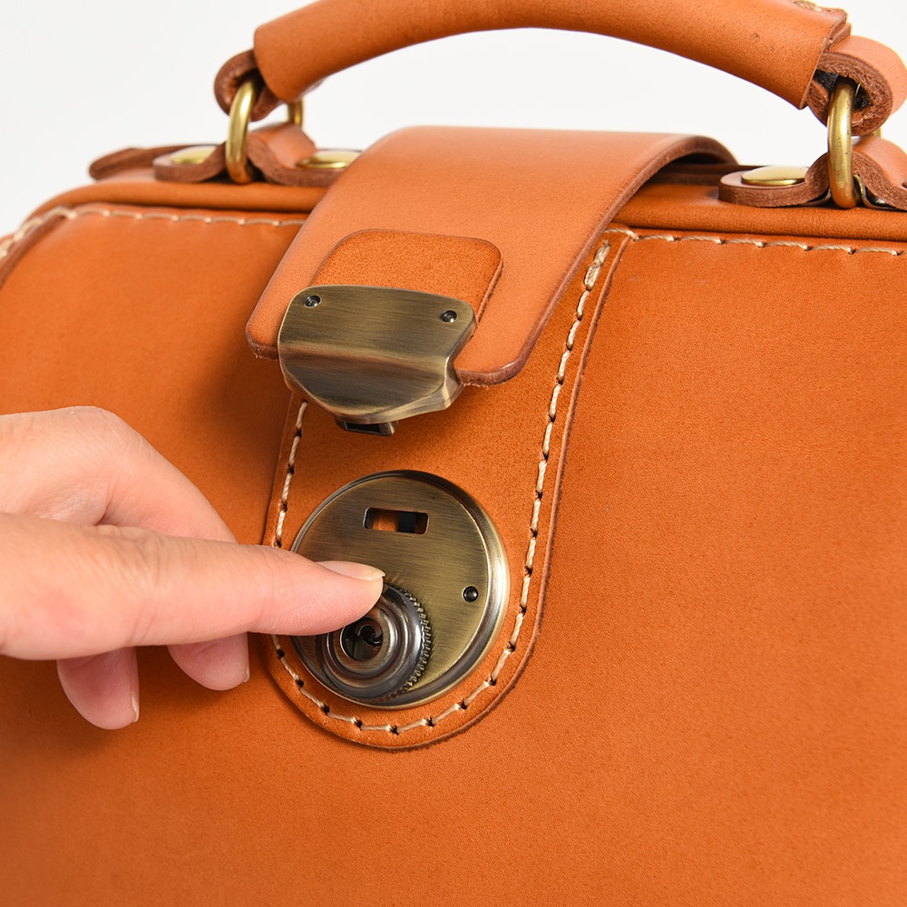 棕色皮革迷你後背醫生包，特寫金屬旋轉鎖扣，手工縫線清晰可見，皮革質感細膩。