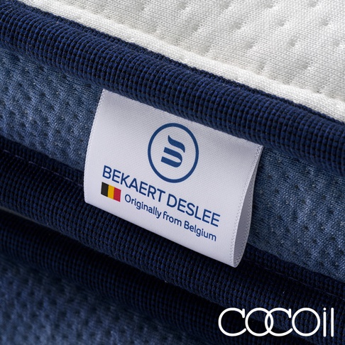專業工藝獨立筒雙層美容床墊的側邊特寫，展示深藍色編織滾邊、白色布標，上面印有「BEKAERT DESLEE」字樣及比利時國旗標誌，以及「Originally from Belgium」字樣。