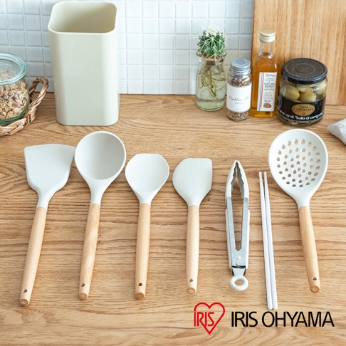 白色矽膠廚房用具組，包含鍋鏟、湯勺、漏勺、夾子及筷子，皆配有木質手柄，整齊擺放在木質桌面上。