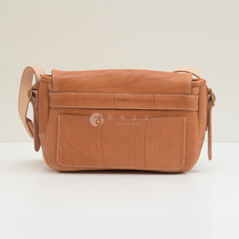 棕色皮革郵差包，帶有翻蓋和金屬扣環。包身設有兩個外部口袋，縫線清晰。肩帶為淺棕色皮革。