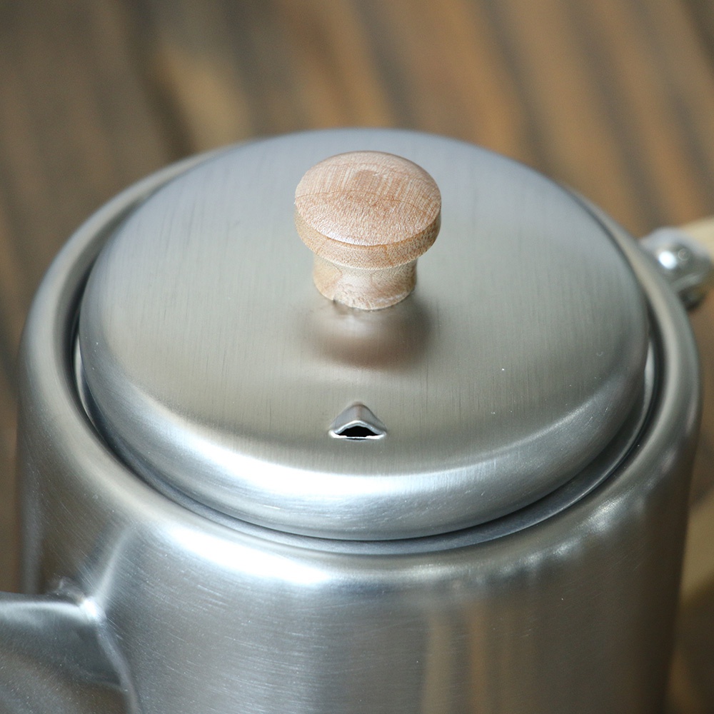 不鏽鋼霧面直筒茶壺，頂部設有木質提鈕，壺蓋中央有透氣孔，整體為銀灰色。