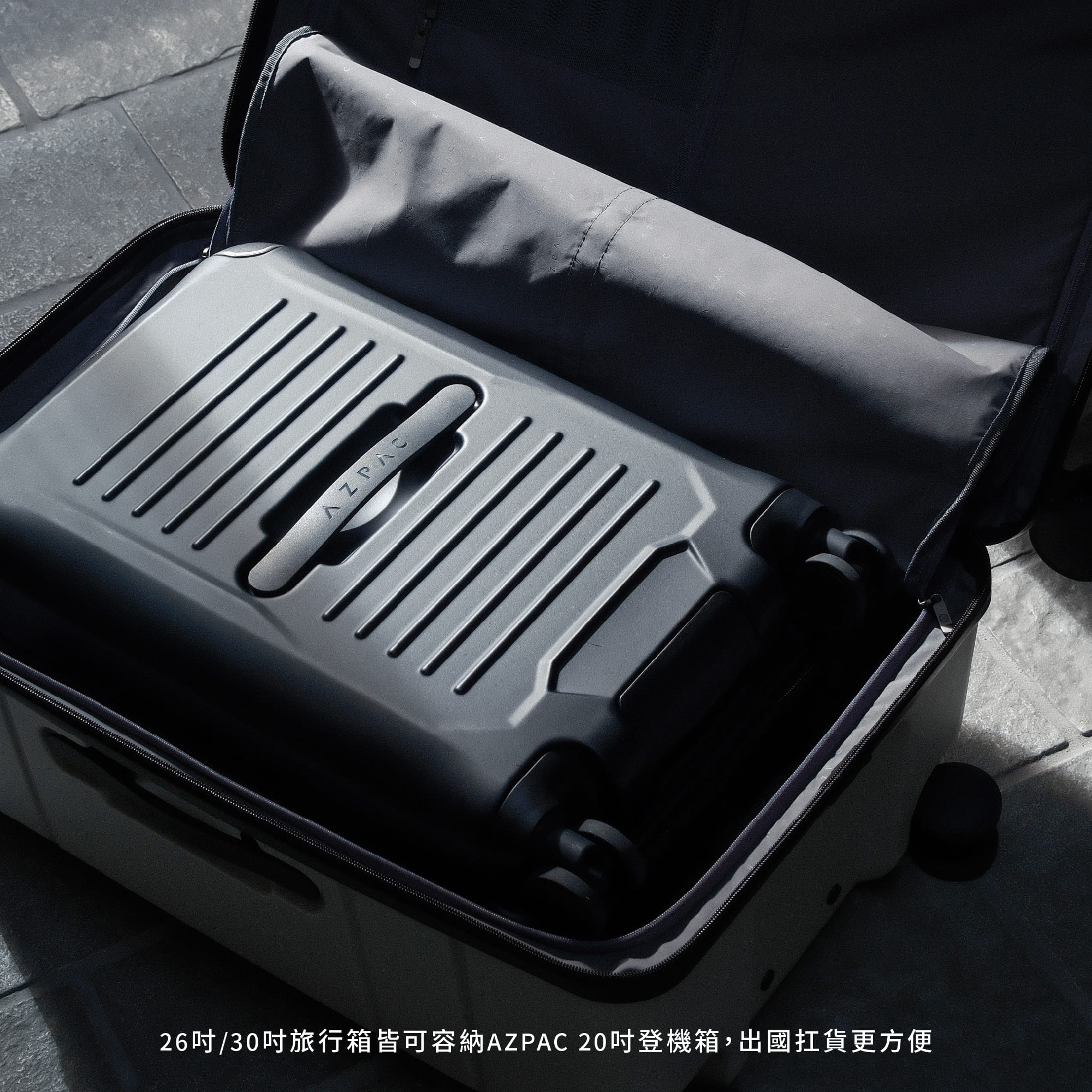 一個打開的米白色大型行李箱，內部整齊放置了一個較小的黑色 AZPAC 二十吋登機箱，展示出大箱容納小箱的收納功能，文字說明二十六吋與三十吋旅行箱皆可容納此款登機箱。