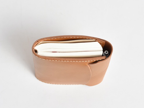 職人手作皮革A6記事本書套，淺棕色皮革，縫線清晰，內含白色紙張的記事本，筆夾處插有一支黑色筆。