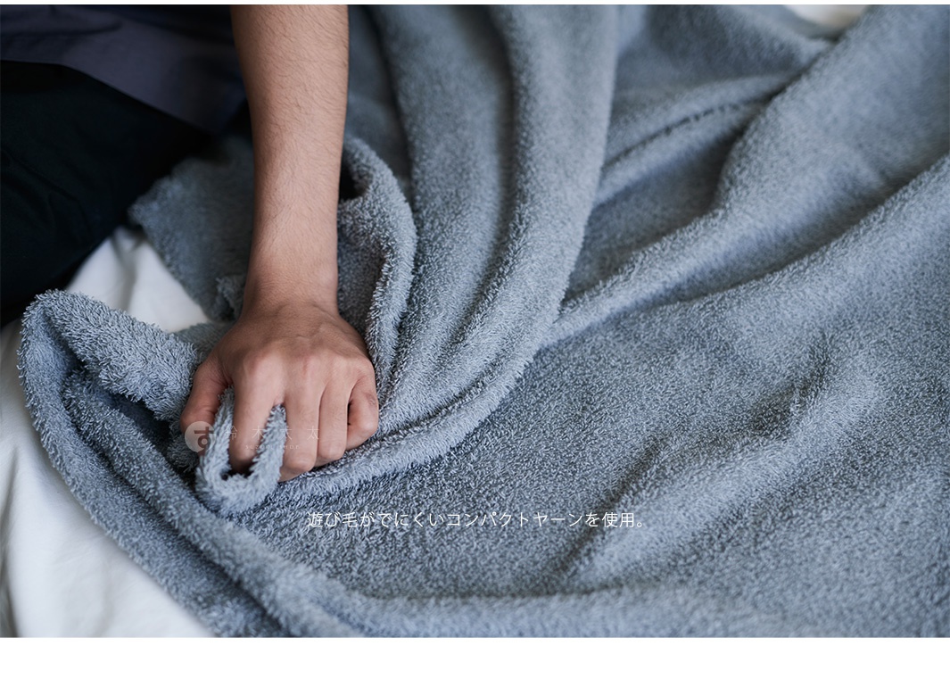 手觸碰灰藍色蓬鬆柔軟的純棉大浴巾，浴巾表面有細微的絨毛感。