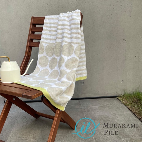 木製摺疊椅上擺放著一條村上綿的條紋與圓點圖案毛巾，旁邊有一個米白色的澆水壺