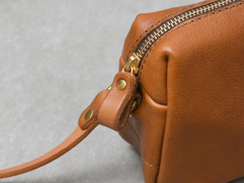 淺棕色皮革製作的拉鍊單肩包，金屬拉鍊與皮革提帶，提帶以鉚釘固定於包身。