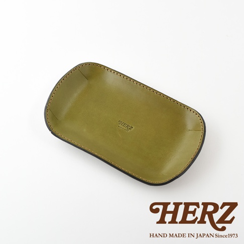 職人手作綠色皮革小物收納盤，邊緣以車縫線裝飾，盤面中央壓印有「HERZ MADE IN JAPAN」字樣。