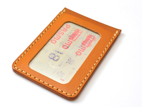 職人手作皮革直式票券收納夾，顏色為棕褐色，材質為真皮，車縫線為米白色。夾內插有一張印有日文「PASMO」字樣的票卡。