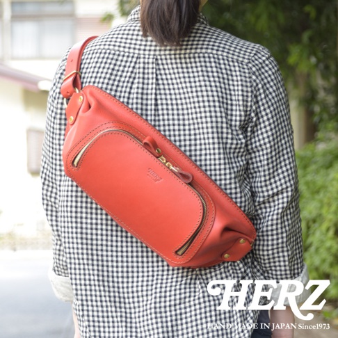日本HERZ 職人手作紅色皮革拉鍊旅行斜背包，印有品牌標誌。
