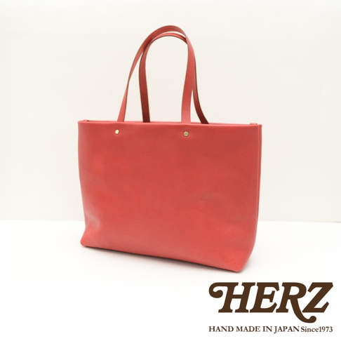 紅色皮革極簡托特包，採用四個口袋設計，配有兩個皮革提把，包面有兩個金色鉚釘裝飾。