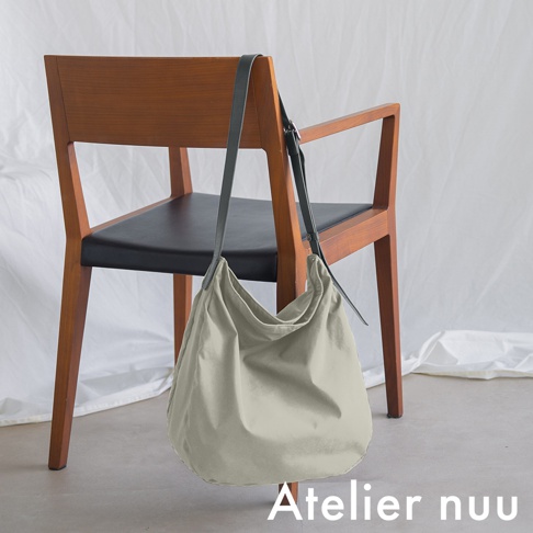 Atelier nuu ssent 肩背托特包，放在木製椅子上的淺色帆布包，包袋一側的肩帶懸掛在椅背上。