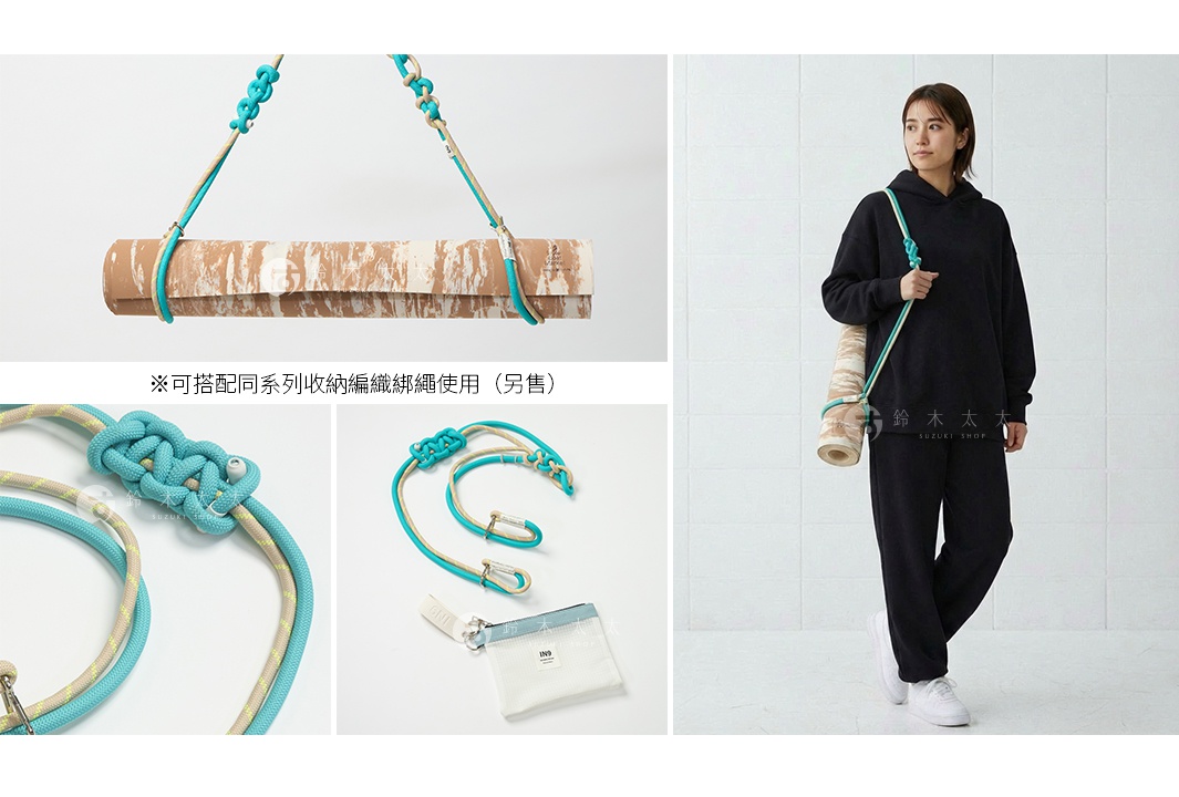 一個女人身穿黑色連帽衫和運動褲，肩上斜挎著一個瑜珈墊，瑜珈墊由藍色和米色的編織繩綁帶固定。