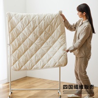 米白色菱格紋羊毛床墊，厚實柔軟，邊緣有細緻滾邊，由一位穿著亞麻睡衣的女性展示。