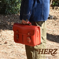 一個紅色皮革製成的兩用單肩包，具有頂部手柄、翻蓋和兩個金屬扣。