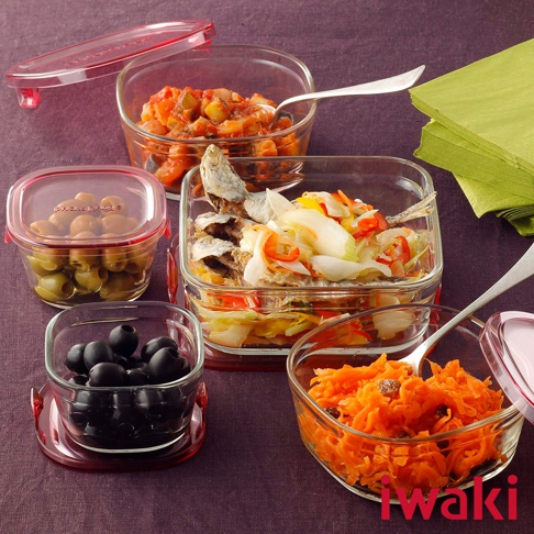 多個透明耐熱玻璃方形保鮮盒，分別裝有蔬菜、魚、橄欖和胡蘿蔔絲，搭配紅色密封蓋，擺放在紫色背景上。