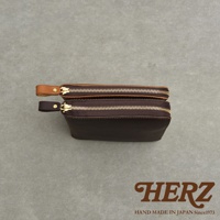 兩款職人手作皮革記事本收納包，一個為棕褐色，另一個為深咖啡色，皆配有金色拉鍊和皮革拉環。