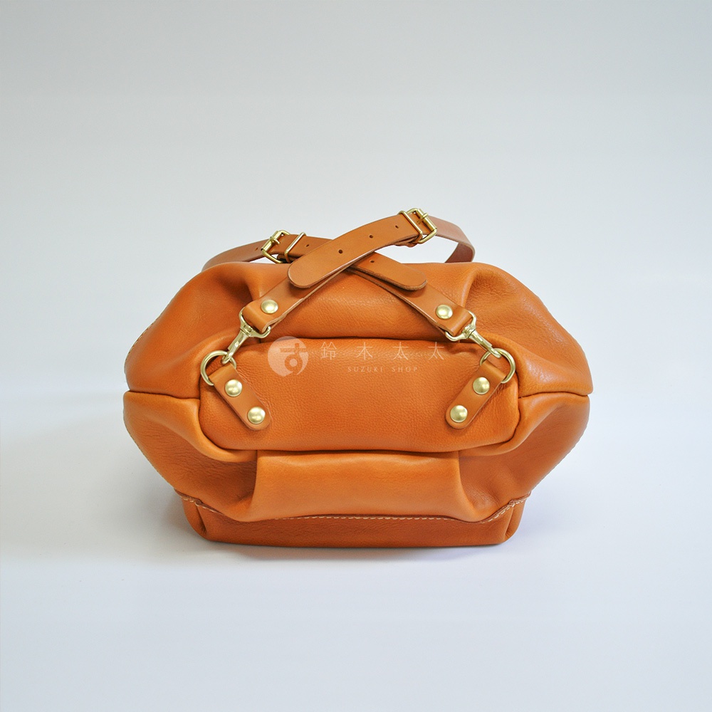 職人手作皮革輕旅行後背包 R-144，焦糖色，柔軟皮革材質，附有兩條可調節式皮質提把，以及可扣合的黃銅金屬配件，整體呈現圓潤飽滿的造型。