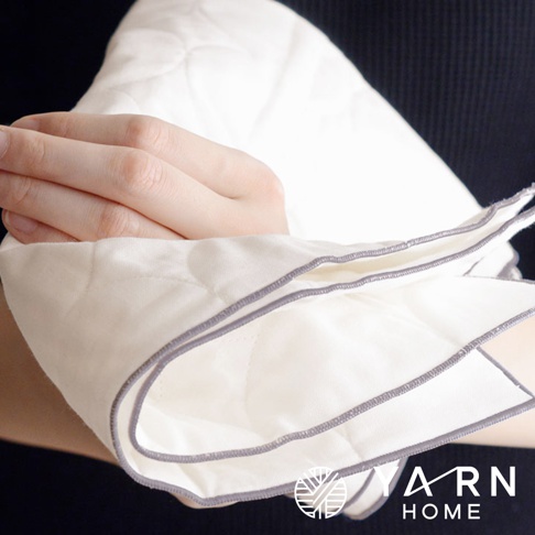 一雙手正拿著一塊米白色、帶有菱形絎縫紋路的廚房拭巾，拭巾邊緣滾有灰色包邊，質地柔軟。