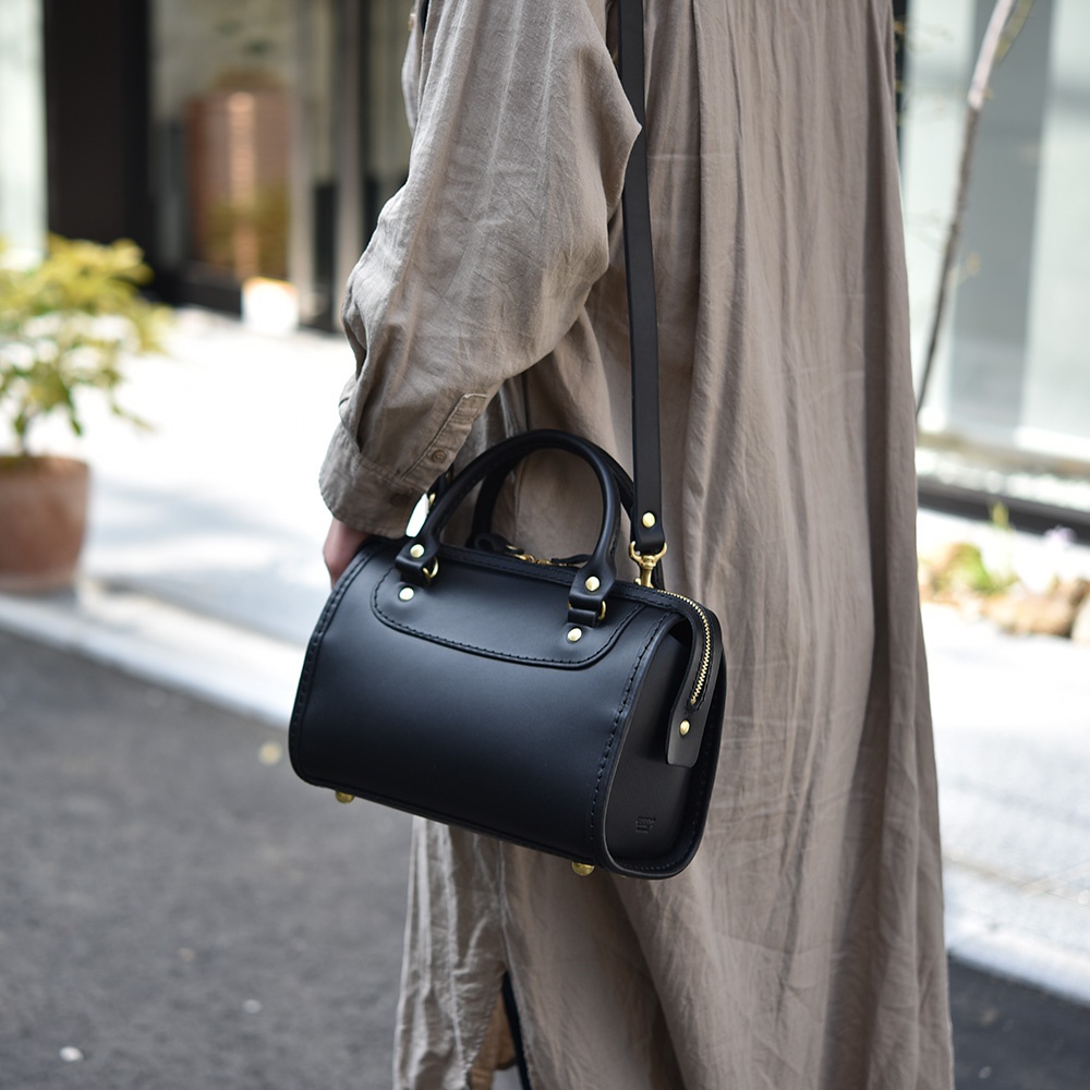 職人手作黑色皮革迷你波士頓包，配有頂部提把、可拆卸斜挎肩帶，以及金色拉鍊與金屬配件。