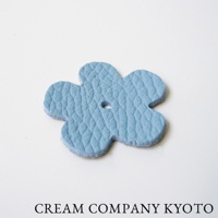 淺藍色皮革製成的五瓣花形小吊飾，表面有壓紋，中央有一個小圓孔。