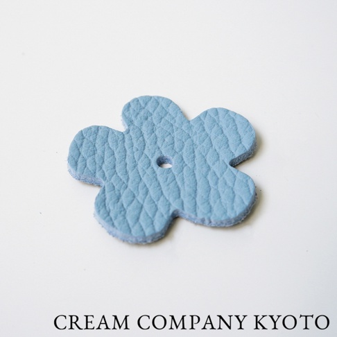 淺藍色皮革製成的五瓣花形小吊飾，表面有壓紋，中央有一個小圓孔。