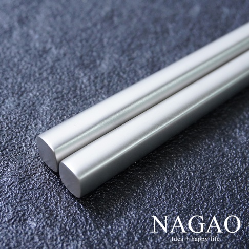 一雙銀灰色不鏽鋼筷子，表面帶有細微磨砂質感，末端呈圓角方形，放置於深灰色紋理背景上。