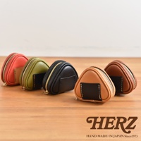 五個職人手作皮革三角飯糰造型小物收納包，顏色分別為橘紅、墨綠、黑色、淺棕色與深棕色，皆配有金色拉鍊，部分款式有黑色皮革裝飾。