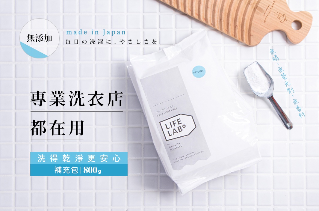 白色無添加洗衣粉補充包，內有銀色金屬勺子裝著白色粉末，背景為白色馬賽克瓷磚，上方有一塊木製的洗衣板。