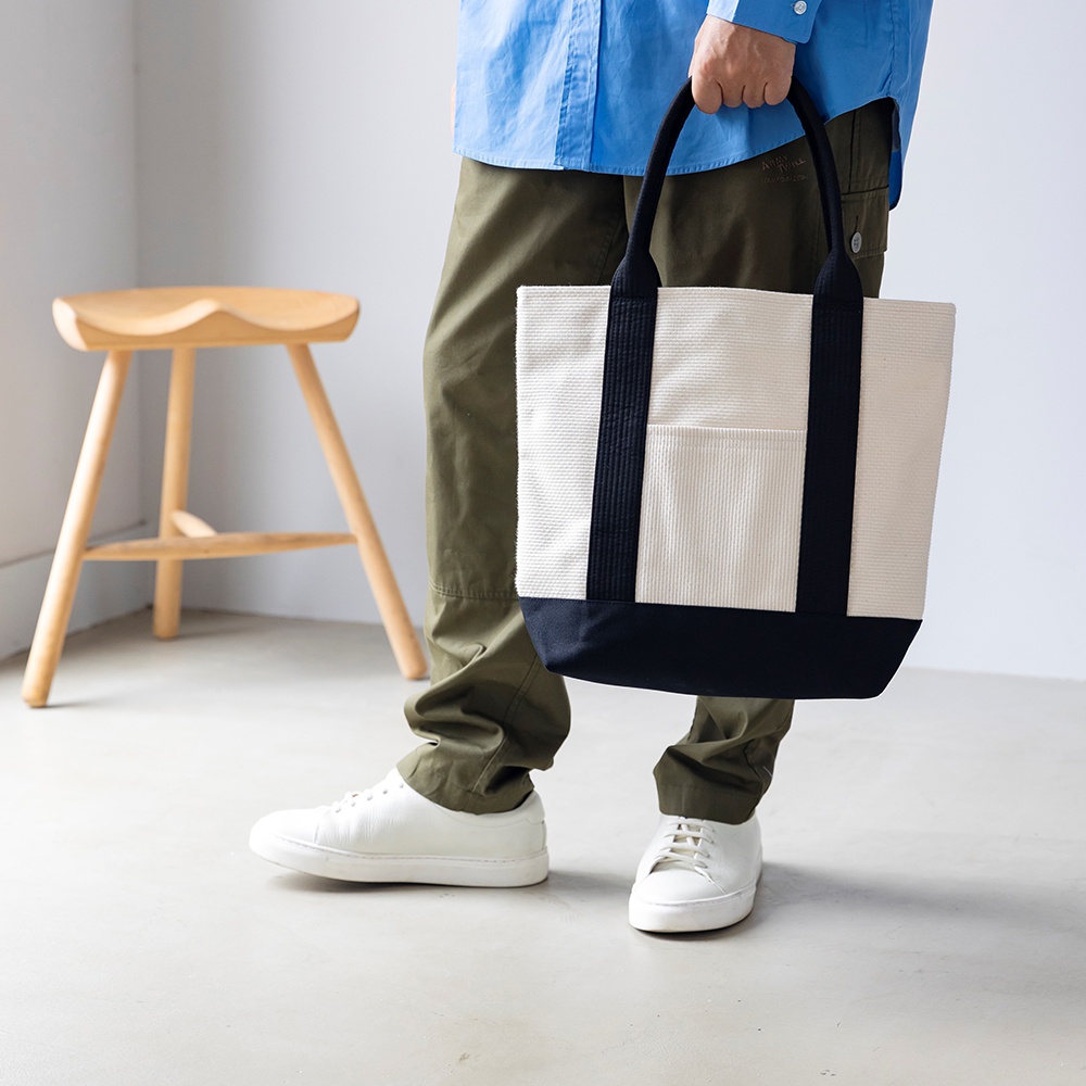 三河木綿刺子織OBI托特包，米白色主體搭配海軍藍底部與黑色織帶提把，正面有兩條黑色直條紋與一個方形口袋。