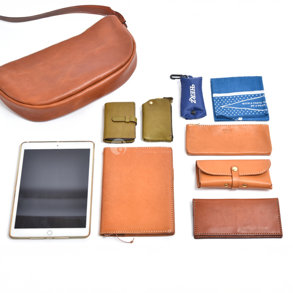 模式B： 一個日本製HERZ皮革馬鞍包，旁邊擺放著一個平板、一個筆記本、一個長夾、一個短夾、一個小零錢包、一條藍色印花手帕，以及一個藍色收納袋。