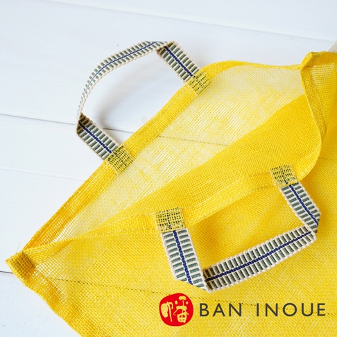 黃色網狀提把蔬果收納袋，提把為織帶材質，帶有藍綠色條紋裝飾，袋身網格清晰，適合透氣保存蔬果。