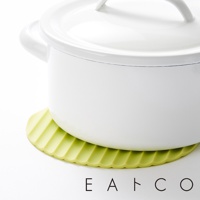 一個淺綠色的圓形隔熱墊，表面有放射狀的溝槽紋理，墊在一個白色金屬鍋的底部，鍋蓋已蓋上，鍋子放在白色背景上。