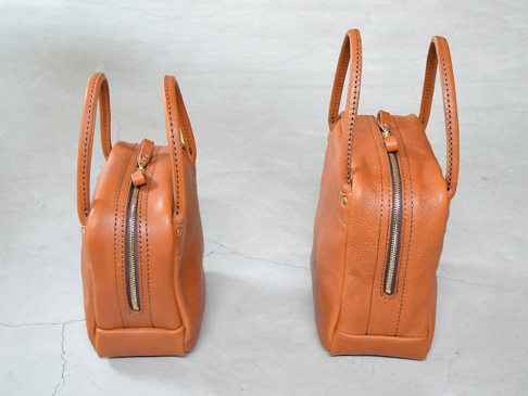 職人手作皮革Organ方形托特包 (G-47) M，呈現經典圓潤方形輪廓，採用棕褐色皮革製作，搭配金色拉鍊與縫線細節，質感厚實，提把設計簡約。