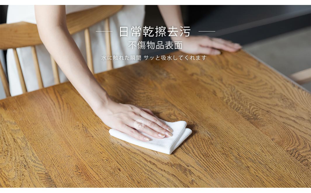 兩條白色超極細纖維擦拭布疊放在木紋桌面上，一隻手正拿著其中一條擦拭桌面。