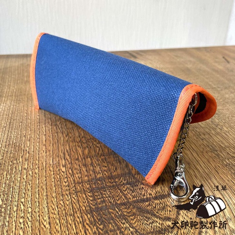 犬印純綿6號帆布眼鏡收納盒，藍色帆布材質搭配橘色滾邊，附有銀色金屬扣環與鏈條，右下角有犬印鞄製作所的品牌標誌。