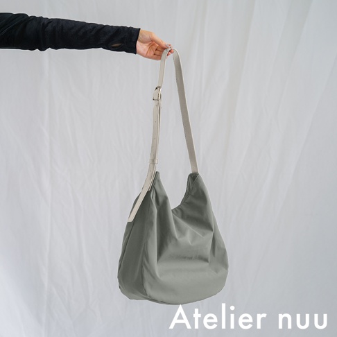 Atelier nuu 品牌 ssent 肩背托特包，米白色織帶搭配灰綠色帆布包身，由手部拿著展示。