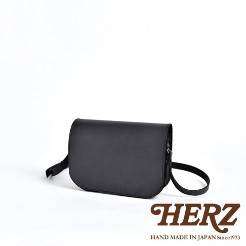 黑色皮革翻蓋橫式單肩包，簡潔設計，附有可調整的斜背帶，展現職人手作質感。