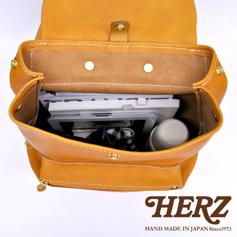 職人手作皮革多口袋後背包 R-135，展示皮革內裡與金屬釦，背包內裝有平板電腦、文件和水杯，呈現芥末黃皮革質感。