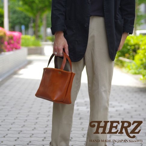 職人手作皮革製的棕色托特包，簡約設計，單肩背帶，包身有兩顆銅色铆釘。